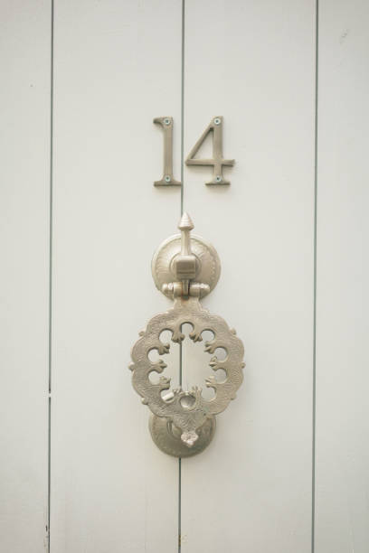 Close-up of an old metallic door knocker on a white wooden door with the number fourteen