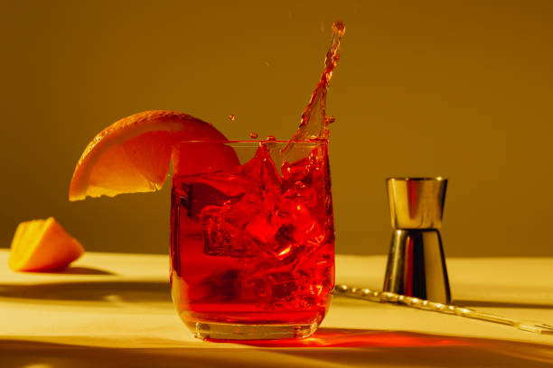 istock Front view of a negroni splashing with orange garnish, bartender tools at sunset with plants shadows 2203479059