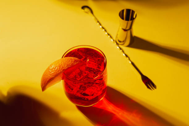 istock Negroni glass with orange garnish, bartender tools at sunset with plants shadows 2203479076