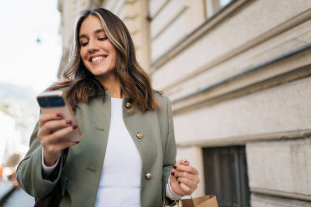 istock Young woman using her phone while walking down the street after shopping 2203479202