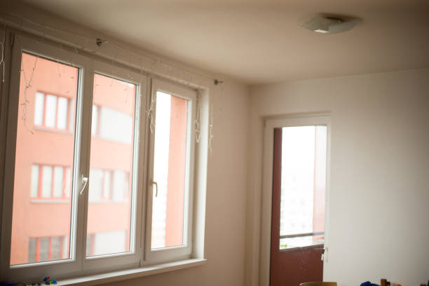 A brightly lit room interior showcases large windows and a door that open to a striking red building backdrop