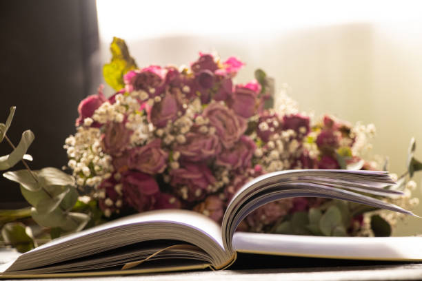 Open book on wooden table at home with dry roses bouquet in room