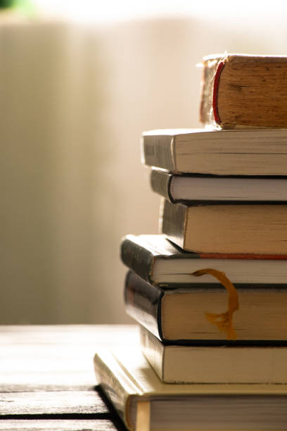A stack of books lies on a wooden table at home, books