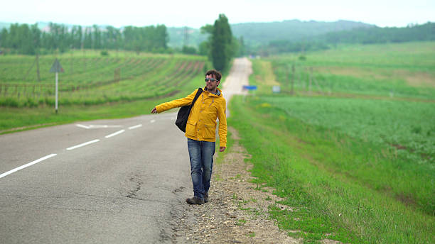 Handsome young man with backpack walking along highway, traveling by autostop. Male tourist hitchhiking in countryside