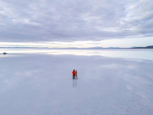 Two people stand on a reflective salt flat, creating a serene, mirror effect. Vast sky and horizon make a peaceful landscape. Ideal for nature, travel, and reflection themes.