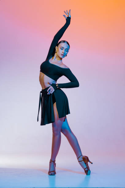 istock Stylish female dancer in black outfit posing in Latin dance move on vibrant gradient studio background. 2203494977