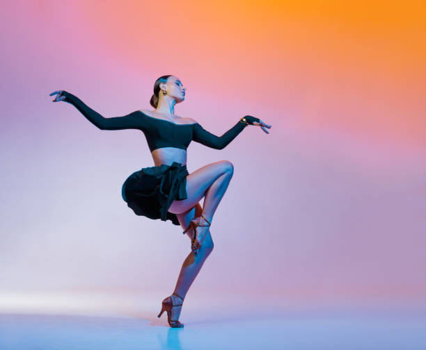 istock Stylish female dancer in black outfit posing in Latin dance move on vibrant gradient studio background. 2203495000
