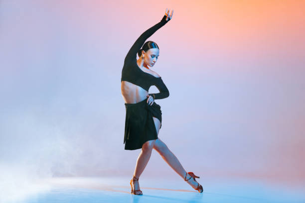 Stylish female dancer in black outfit posing in Latin dance move on vibrant gradient studio background.