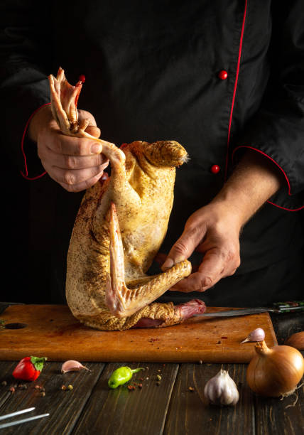 istock A chef skillfully handles a whole duck, preparing it for cooking on a wooden cutting board in a kitchen. Fresh ingredients like garlic and onion are nearby 2203496207