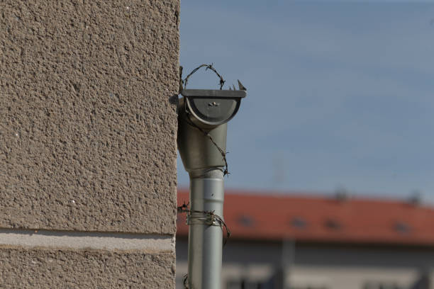 A drainpipe is securely attached to the outside wall on the side of a building, providing essential drainage function and maintenance access