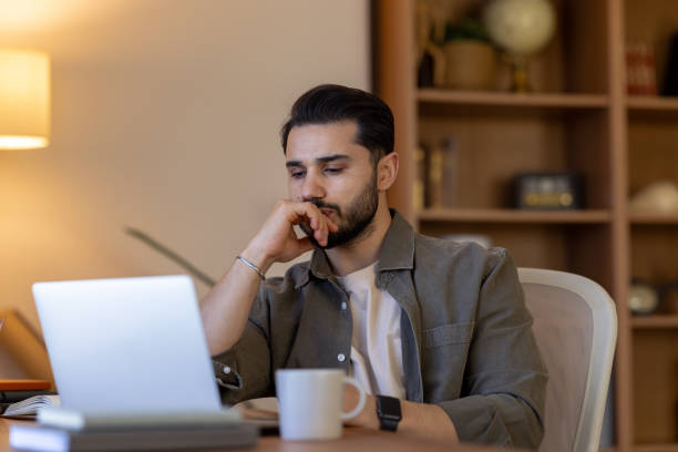istock Young man concentrating while working from his home office, looking at his laptop 2203497570