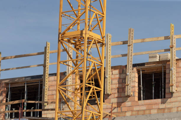 A bright yellow crane is prominently positioned in front of a large building that is currently undergoing construction work and development