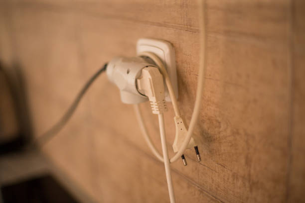 Three electrical cords plug into a single outlet, set against a rustic wooden wall backdrop