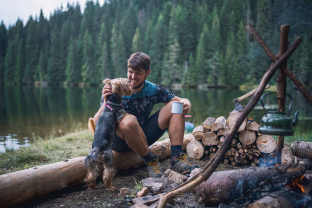 Man on camping playing with his pet terrier dog at the campfire surrounded by the beauty of nature.
