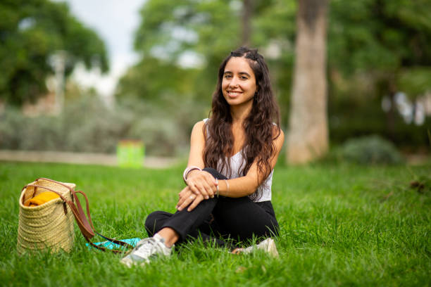 istock smiling young woman sitting on grass in park 2203511027