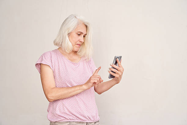 istock Elderly caucasian female using smartphone while standing against white 2203522686