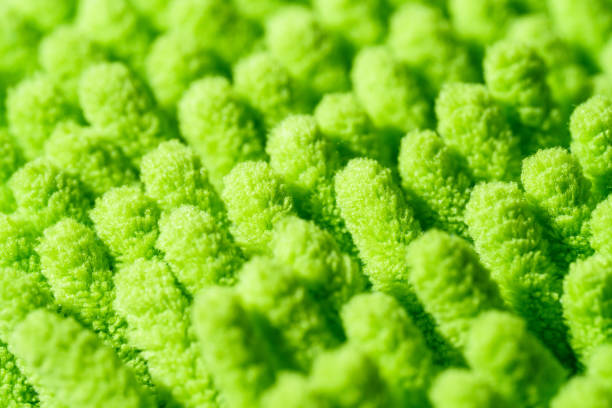 A macro close-up of a green microfiber cleaning cloth, showcasing its soft and fluffy texture. The intricate fibers create a highly absorbent and detailed surface, commonly used for dusting and household cleaning.