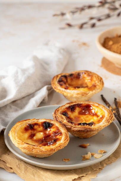 istock Three Pastel de Nata, Portuguese custard tarts, are presented on a plate with cinnamon and vanilla beans. 2203525415