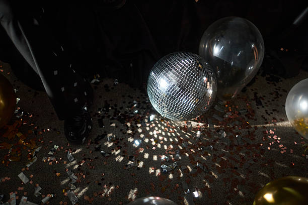 Mirror ball reflecting light onto dance floor scattered with confetti and party balloons creating festive atmosphere during celebration night