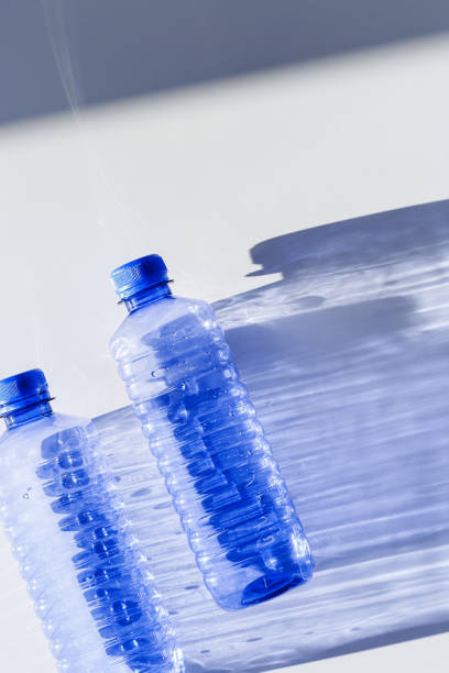 istock Blue plastic water bottles on white blue background with sunlight shadow and sun flare, Minimal top view photo, themes of ecology, recycling, sustainable living, reduce disposable plastics 2203533932