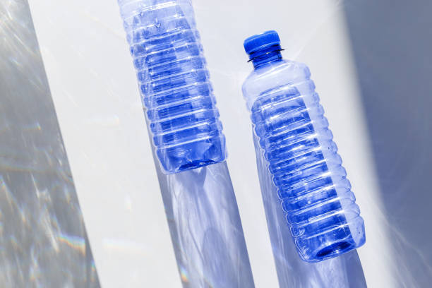 istock Transparent plastic bottles with blue caps and sun shadows on light background. Top view Water bottles at natural light. Themes of recycling, sustainability, water conservation, minimal style 2203533935