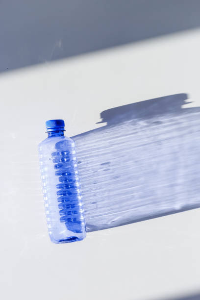istock Blue plastic water bottles on white blue background with sunlight shadow and sun flare, Minimal top view photo, themes of ecology, recycling, sustainable living, reduce disposable plastics 2203533937