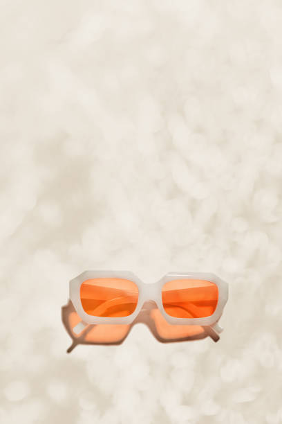 Stylish peach orange colored sunglasses on beige background, copy space, shadow and glare at sunlight, summer fashion white transparent-framed glasses. Minimal aesthetic beach vibes, summer concept