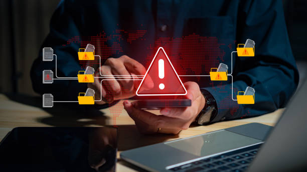 istock A warning alert icon signals a hacked document system as a man types on a keyboard, surrounded by digital files and documents, with a red cybersecurity threat alert prominent in the scene. 2203543683