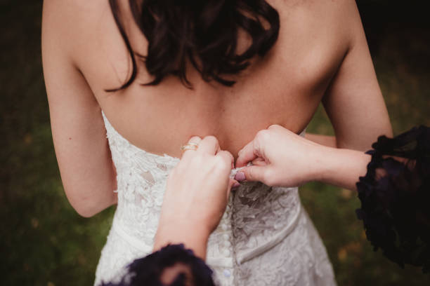 Mother of the bride zipping up bride's wedding dress close up