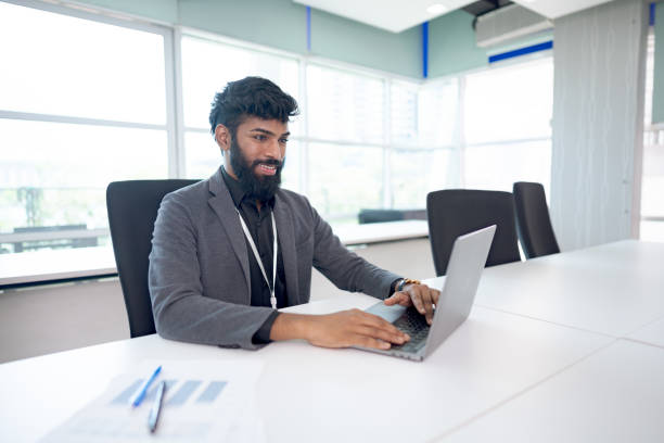 istock Smiling businessman in a suit working on a laptop in a modern office setting with large windows and a bright atmosphere 2203551643