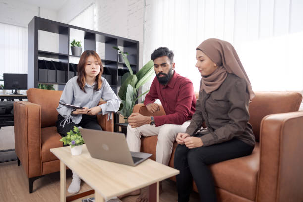 istock Three diverse colleagues engaged in a serious discussion seated on sofas around a laptop in a modern office setting 2203552123