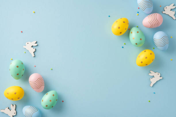 istock Colorful pastel Easter eggs scattered with wooden bunny shapes on a light blue backdrop 2203556806