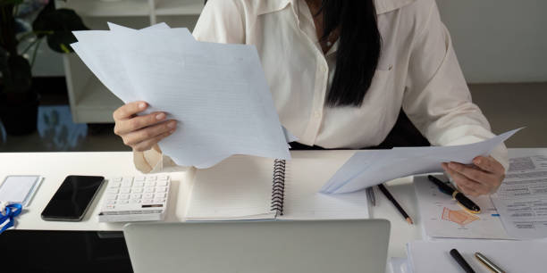 istock Tax Document Organization. An individual comparing tax documents and notes at their desk, ensuring thorough preparation for analysis. 2203558636