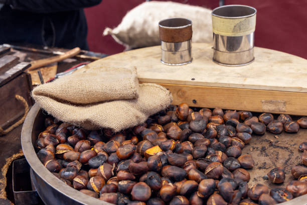 istock Metal roasting pan filled with freshly roasted chestnuts burlap sacks rest on top while metal measuring cups sit on a wooden board in a traditional street food setup 2203561704