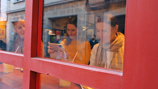Waitress taking orders from a lively group of young people gathered around a table in a trendy cafe, viewed through the window, capturing the vibrant atmosphere of urban dining