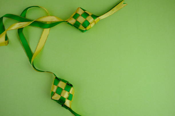 istock hand crafted ketupat or rice dumpling packaging from ribbon isolated on green background. Ramadan and Hari Raya Eid al-Fitr decoration for template, card, and background 2203563038