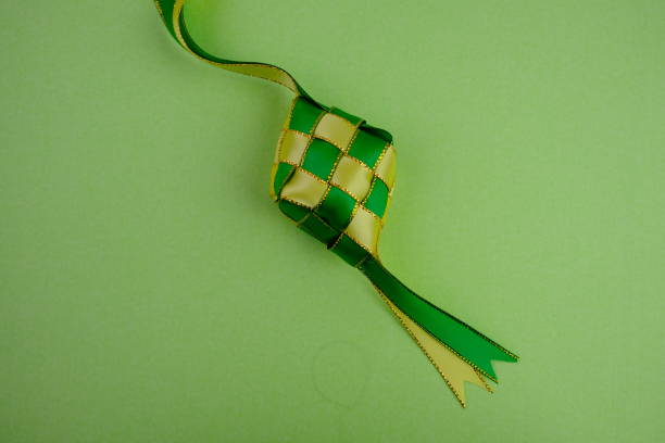 istock hand crafted ketupat or rice dumpling packaging from ribbon isolated on green background. Ramadan and Hari Raya Eid al-Fitr decoration for template, card, and background 2203563073