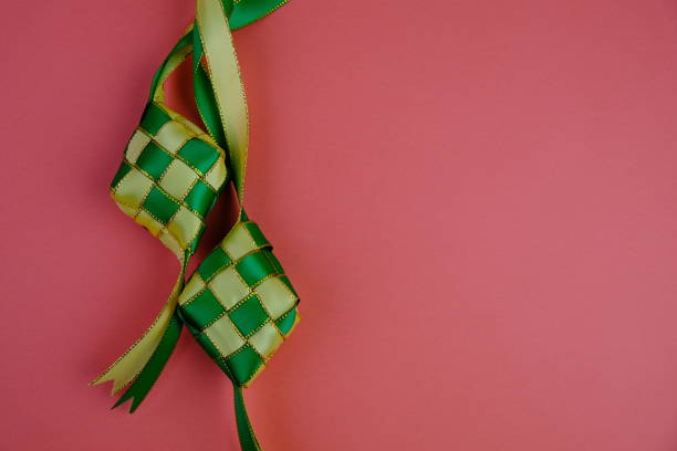istock hand crafted ketupat or rice dumpling packaging from ribbon isolated on green background. Ramadan and Hari Raya Eid al-Fitr decoration for template, card, and background 2203564382