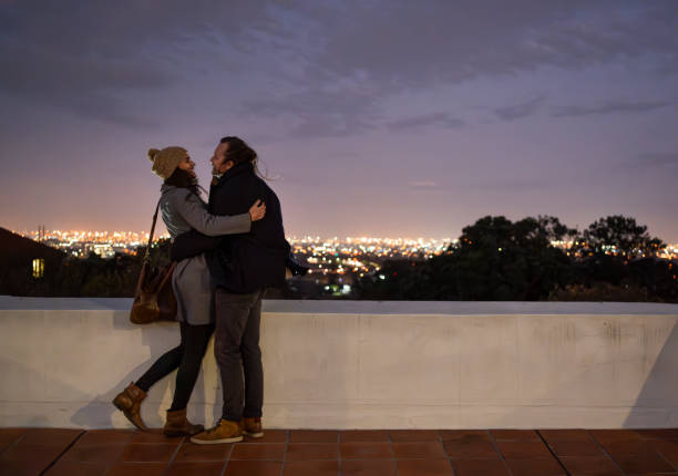 Young couple embracing at a city rooftop during dusk, overlooking the glowing cityscape