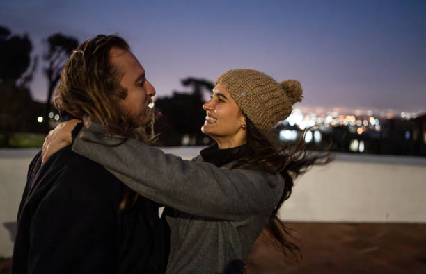 Young couple standing at a rooftop during dusk with glowing cityscape in background