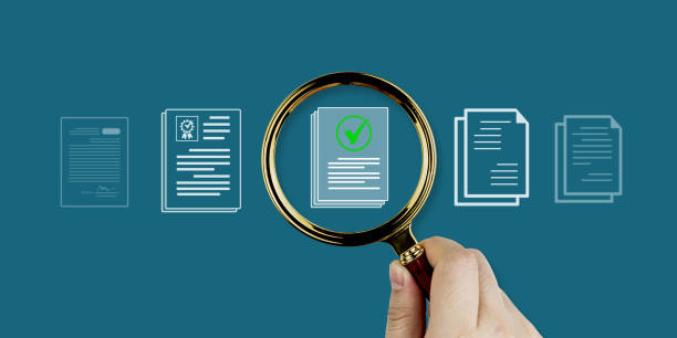 istock A hand holds a magnifying glass focusing on a document icon with a checkmark. Document search system concept. 2203567713