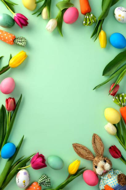 istock Happy Easter concept. Flat lay composition with tulips, colorful Easter eggs, carrots, bunny on green background. Easter frame, vertical banner design 2203568390
