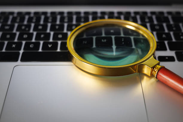 istock Magnifying glass hovering over a laptop keyboard, symbolizing a search for online documents 2203576433