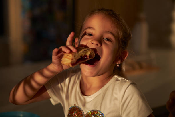 Cute little girl reaching for tasty dessert at white table against pink background