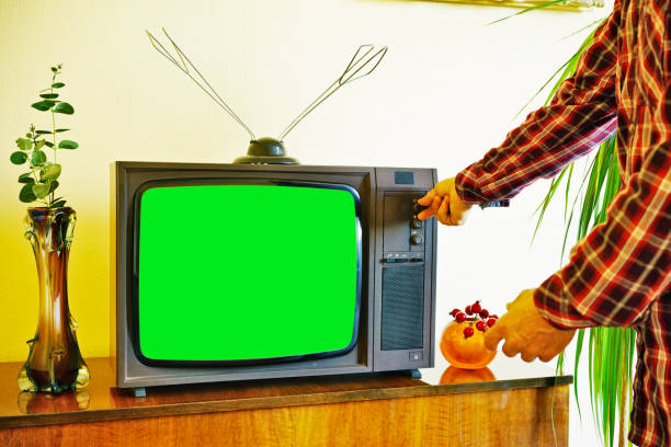 Hands of a man turning on a vintage tube TV set with a green screen and home antenna on it.