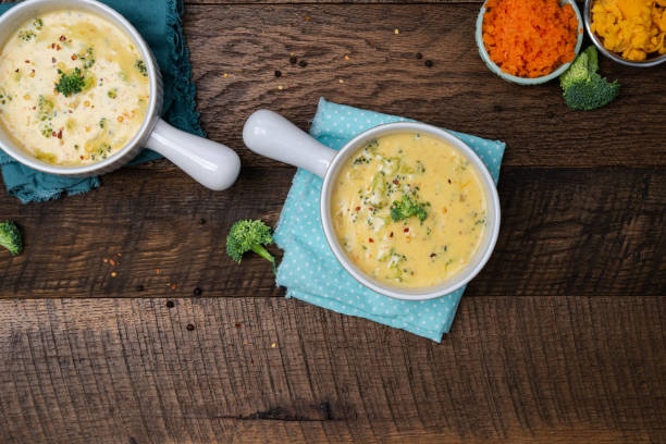 istock Creamy, Broccoli cheddar soup in white bowls with handle on a walnut table background with blue napkins. 2203591650