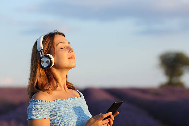 Woman meditating in a lavender field using headphone and phone stock photo