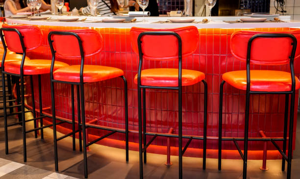 istock Bright red and orange bar stools line a modern counter, creating a cheerful atmosphere for patrons. The inviting setup encourages laughter and socializing in a stylish venue 2203598736