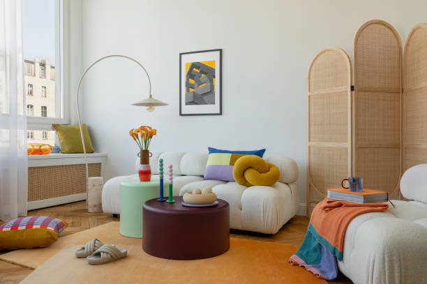 istock Bright and cozy living room with a white sofa, colorful pillows, and playful decor elements. A large window and minimalist lighting create a serene and inviting space. 2203599269