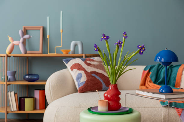 istock Modern living room with playful decor accents. A cozy sofa adorned with a patterned cushion, vibrant vases, and a blue lamp, complemented by fresh irises in a bold red vase. 2203602301